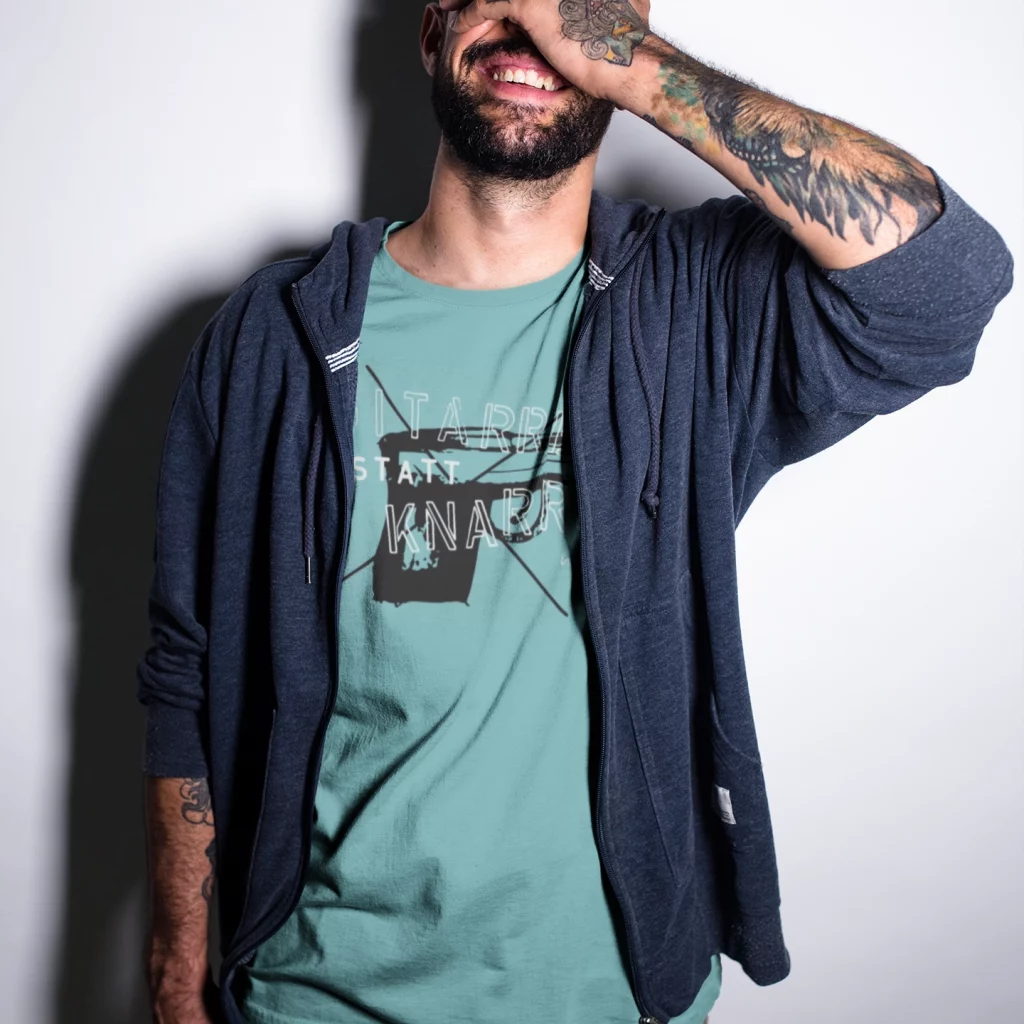 Ein tätowierter Mann trägt das türkise Shirt von Gitarren statt Knarren